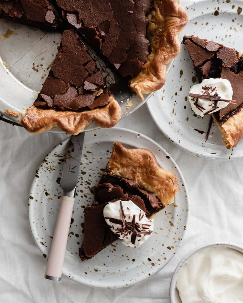 Slices of fudgy dark chocolate chess pie on plates and topped with whipped cream