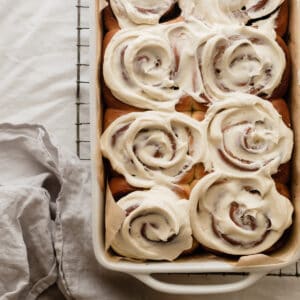 A pan of 8 cinnamon rolls topped with cream cheese frosting sitting on top of a cooling rack