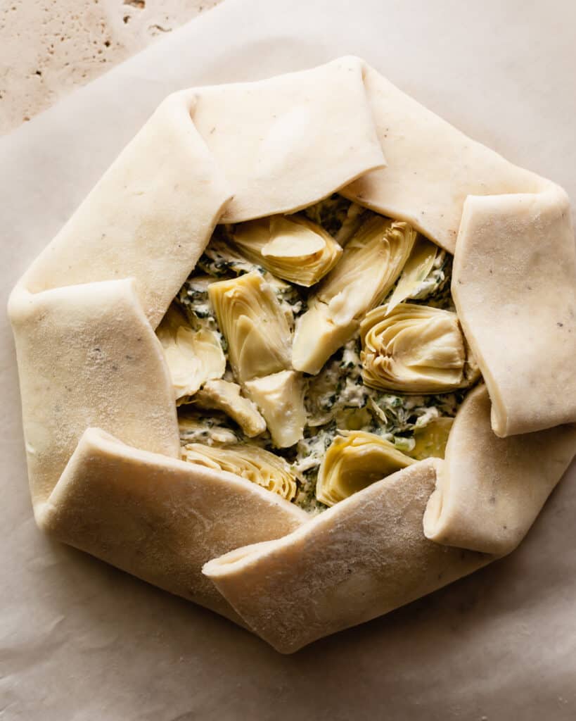 Overhead shot of a galette crust filled with spinach and artichoke dip with the crust overlapping and folded over