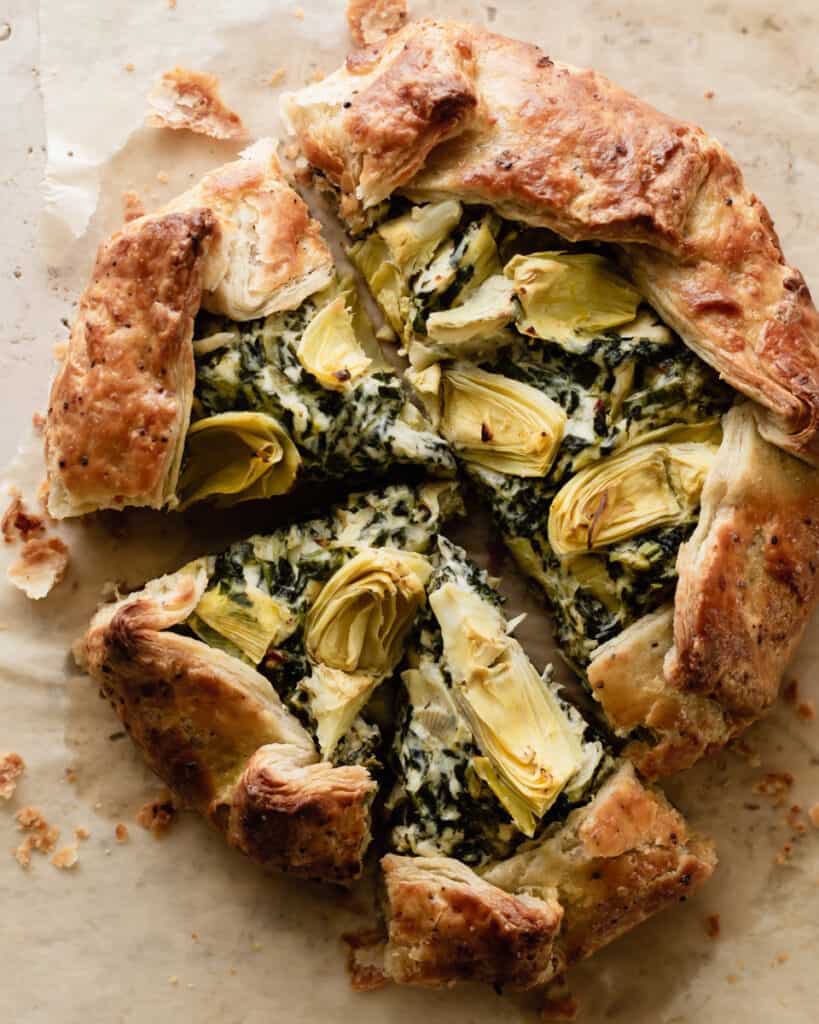 Overhead shot of a savory galette filled with spinach and artichoke dip sitting on parchment paper