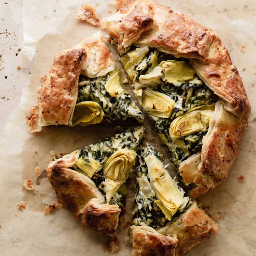 Overhead shot of a savory spinach and artichoke galette sitting on parchment paper